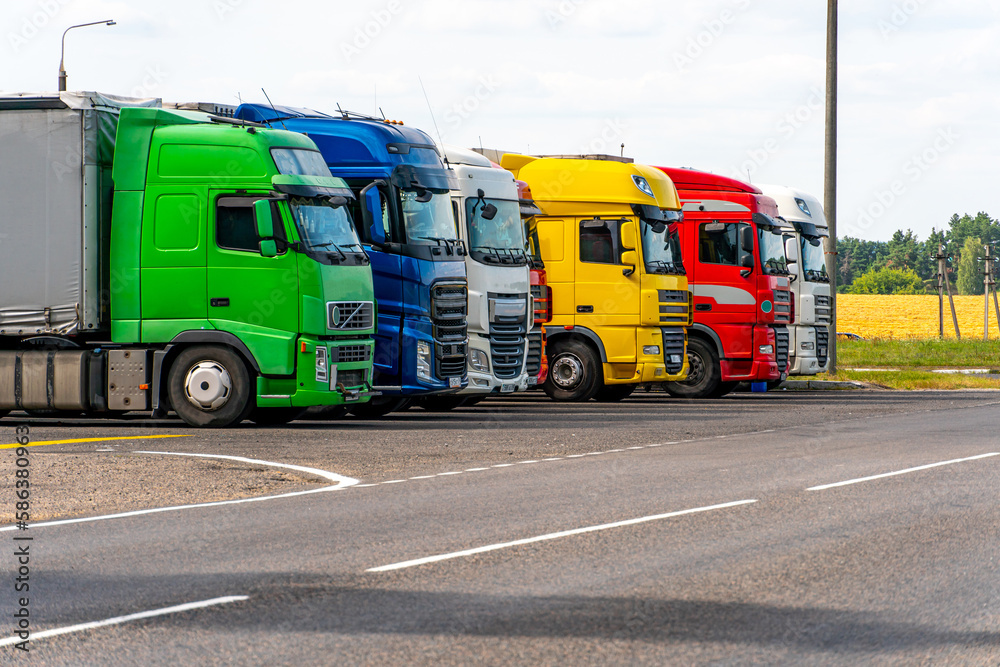 Trucks with containers in the parking lot along the highway against the background of clouds. The concept of logistics, transport and cargo transportation. The resting place of trucks in the parking