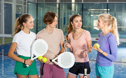 Portrait of four tennis players of different ages standing with padel rackets indoors, discussing topical issues of the ..upcoming game on the court © JackF