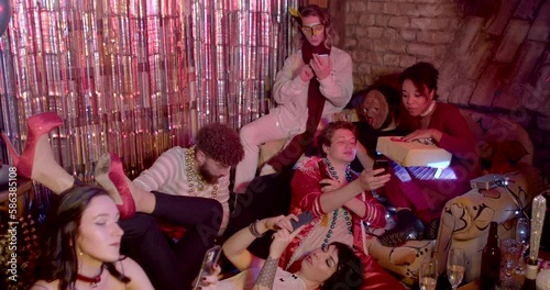 Young people use phones during party. No being physically and emotionally involved in company. Text messages while hangout with friends, online texting to detriment of live communication. Slow motion.