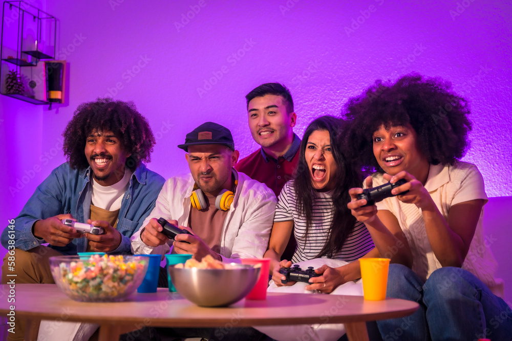 Adult party. Young people sitting on the sofa playing video games with popcorn. Joystick or controller in hand, purple led Adult party. Young people sitting on the sofa playing video games with popcorn. Joystick or controller in hand, purple led