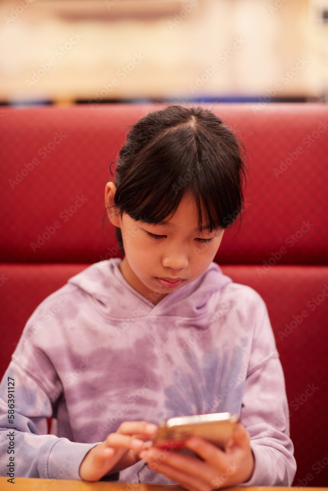 外食の店でスマホを見ている小学生の女の子の姿 外食の店でスマホを見ている小学生の女の子の姿