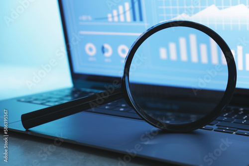 Magnifying glass on keyboard of laptop against light background, closeup
