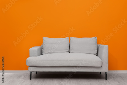 Comfortable sofa near bright orange wall indoors