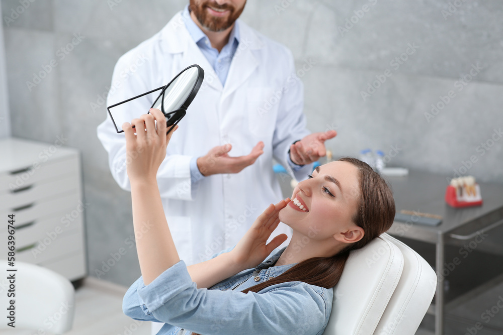 Fototapeta premium Young woman looking at her new dental implants in mirror indoors