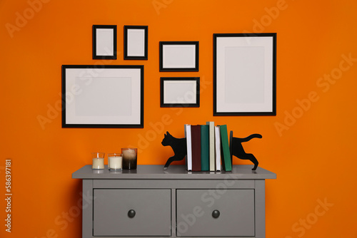 Empty frames hanging on orange wall in room above chest of drawers with decorative elements. Mockup for design © New Africa