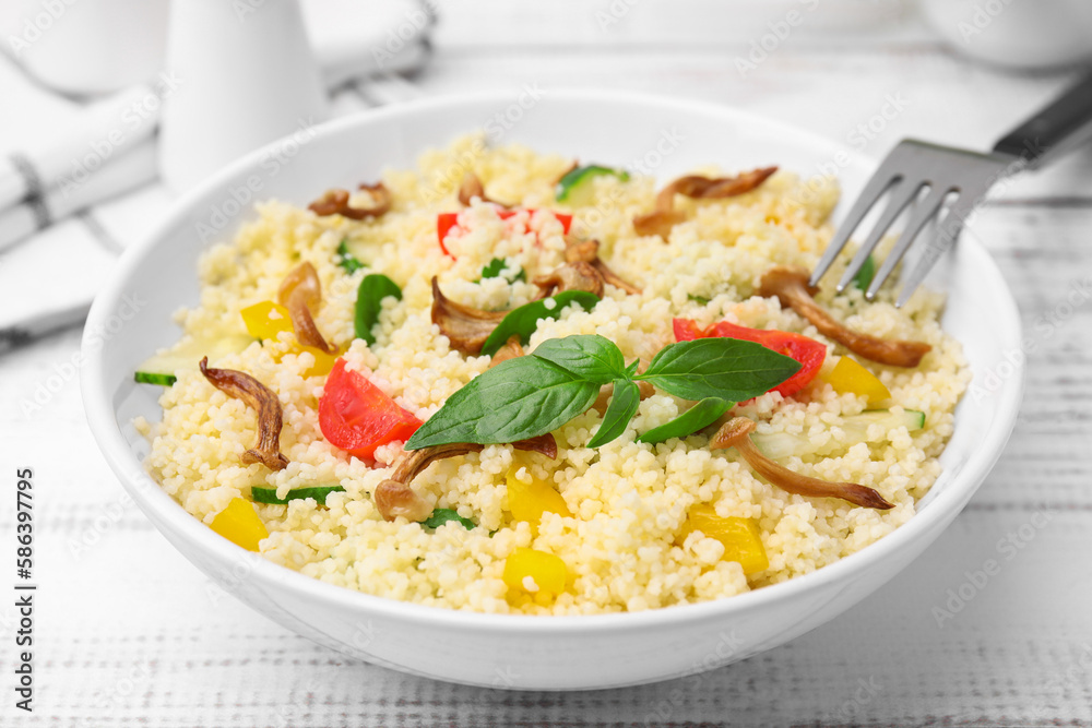 Bowl of delicious couscous with vegetables and basil served on white wooden table, closeup Bowl of delicious couscous with vegetables and basil served on white wooden table, closeup
