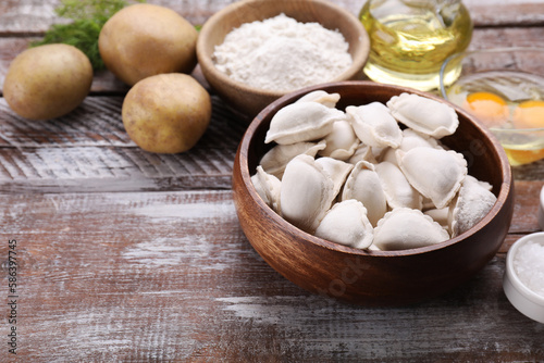 Raw dumplings (varenyky) and ingredients on wooden table, space for text