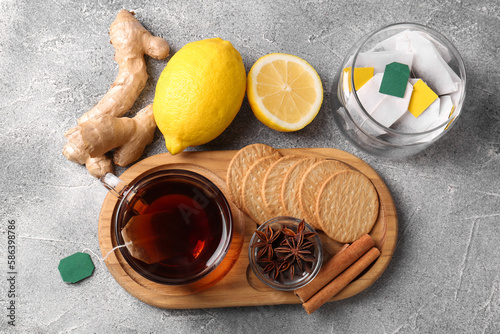 Tea bags, cup of hot drink, cookies and ingredients on light grey table, flat lay