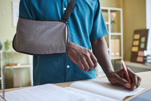 Tableau sur toile Close up of black man with arm sling working at standing desk in office and writ