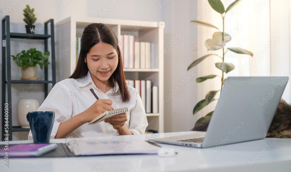 Smiling female entrepreneur taking notes, making business plans on notebook and using laptop at workplace. Smiling female entrepreneur taking notes, making business plans on notebook and using laptop at workplace.