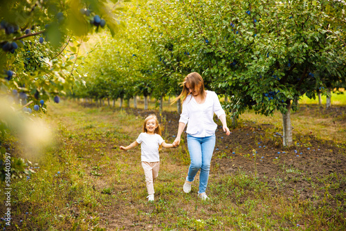 Mother and daughter are playing and running around a plum orchard on a beautiful morning. © Viorel