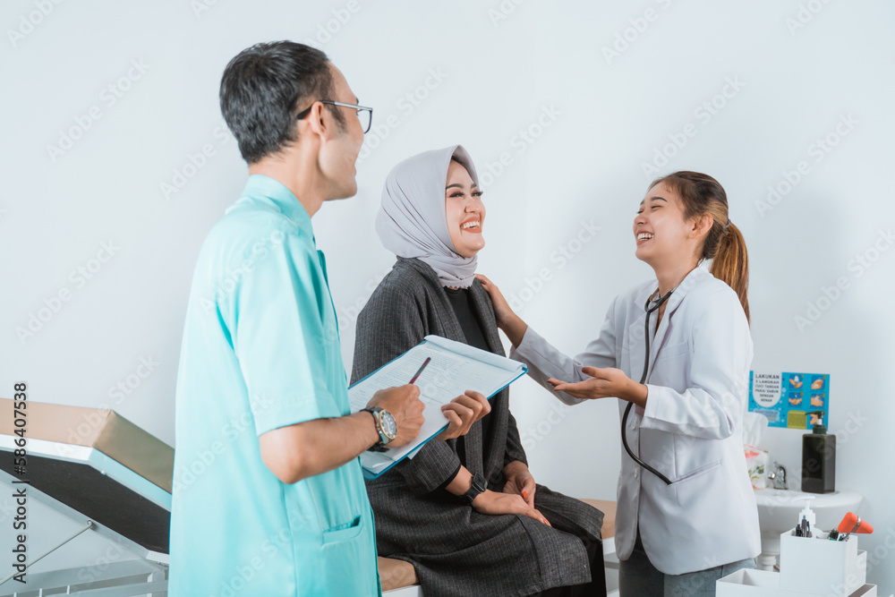 Obraz premium a beautiful doctor beautiful patient and the handsome nurse laughing together while doing medical check up for the female patient that sitting on the bed