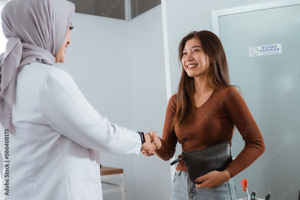 Obraz premium a female patient in brown clothes hand shake with the female doctor in doctor's coat inside the medical checkup room