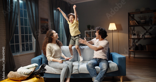 Tableau sur toile Excited naughty, noisy Asian child jumping around mom and dad on sofa, shouting, annoyed