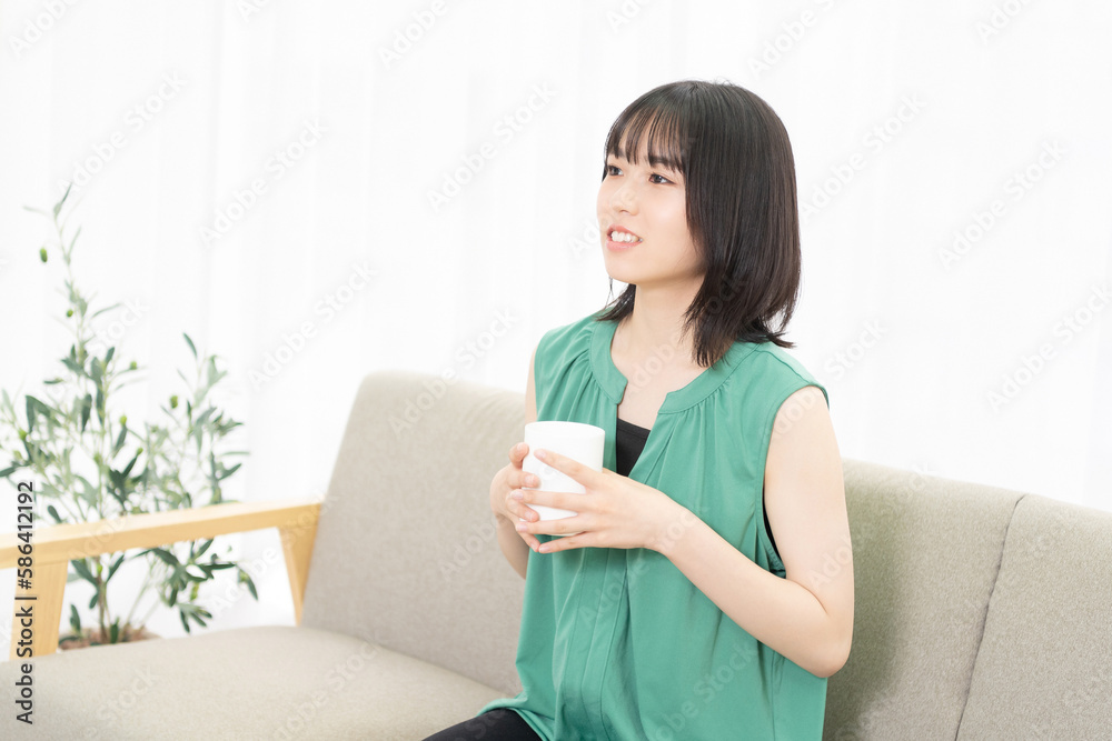 ソファーに座ってコーヒーを飲む若い女性 ソファーに座ってコーヒーを飲む若い女性