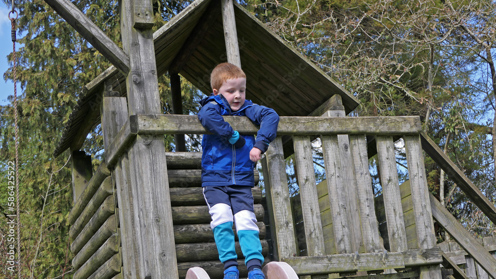 Redhead boy having fun playing on in a treehouse and swings at a Playpark on sunny day Redhead boy having fun playing on in a treehouse and swings at a Playpark on sunny day