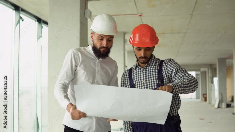 Indian architect and supervisor meeting at construction site. Multiethnic manual worker and engineer discussing on plan. Two construction workers working together while visiting a new building