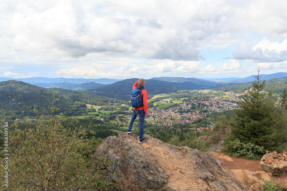 Male hiker (man) standing on mountain Silberberg and looking at panorama of municipality Bodenmais in Bavarian Forest, Germany