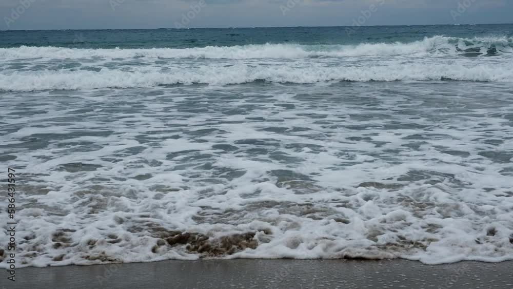 Slow motion of foamy waves falling towards sand beach under low the sunlight Slow motion of foamy waves falling towards sand beach under low the sunlight