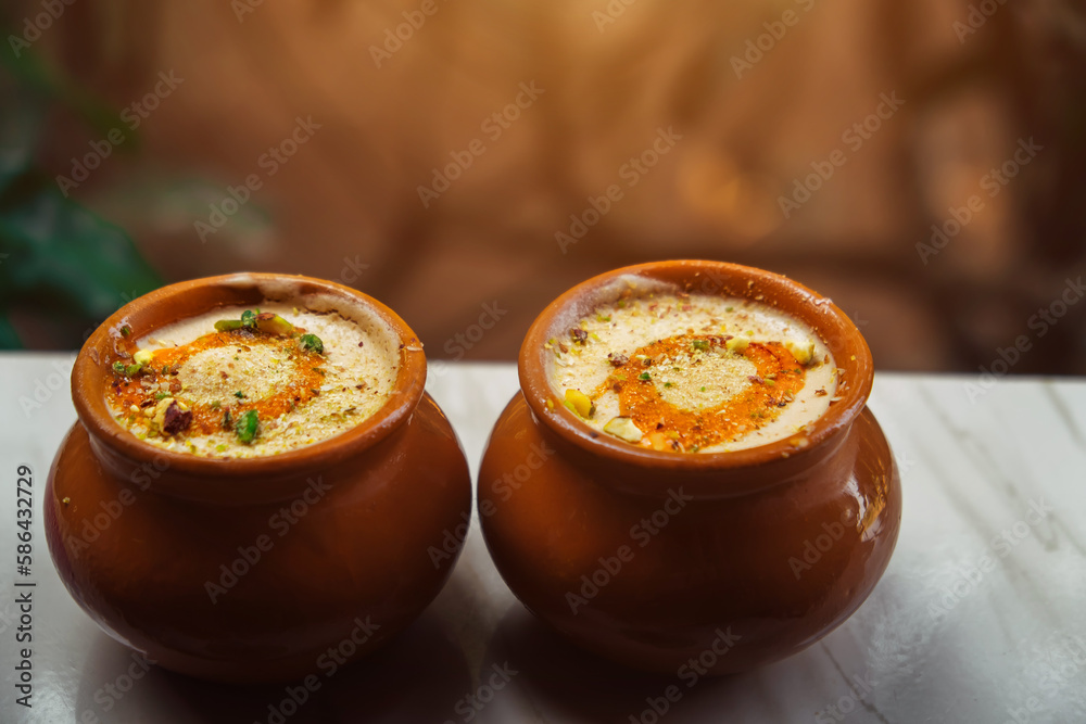 Kulfi or Qulfi ice cream in a clay pot. Kulfi is a popular traditional Indian dessert made of milk with spices and nuts. Two clay pots with ice cream on a blurry background - obrazy, fototapety, plakaty 