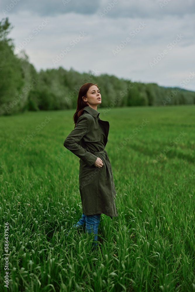a beautiful woman in a dark coat stands in a green field in the spring in rainy weather a beautiful woman in a dark coat stands in a green field in the spring in rainy weather