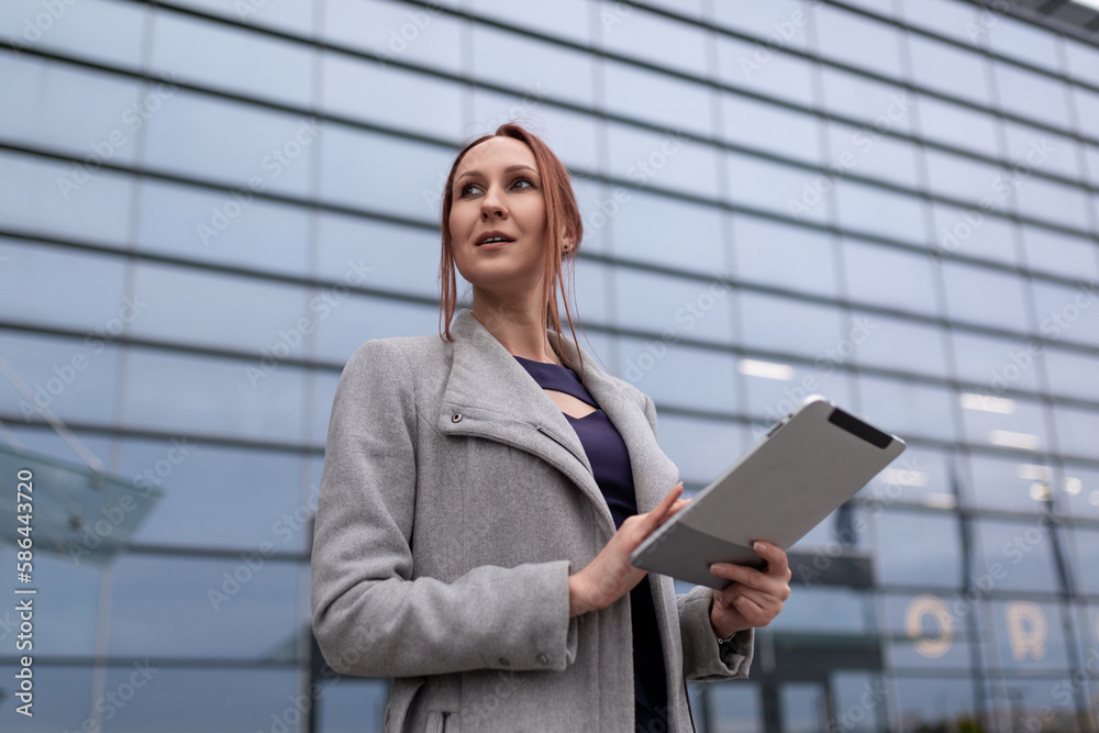 young woman designer with a ponytail hairstyle holds a tablet on the background of a large glass building young woman designer with a ponytail hairstyle holds a tablet on the background of a large glass building