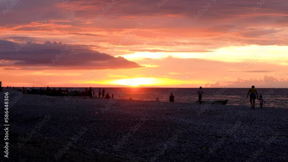 Timorese families walking along the beach and fisherman with fishing boats with beautiful sunset in capital Dili, Timor Leste, Southeast Asia Timorese families walking along the beach and fisherman with fishing boats with beautiful sunset in capital Dili, Timor Leste, Southeast Asia