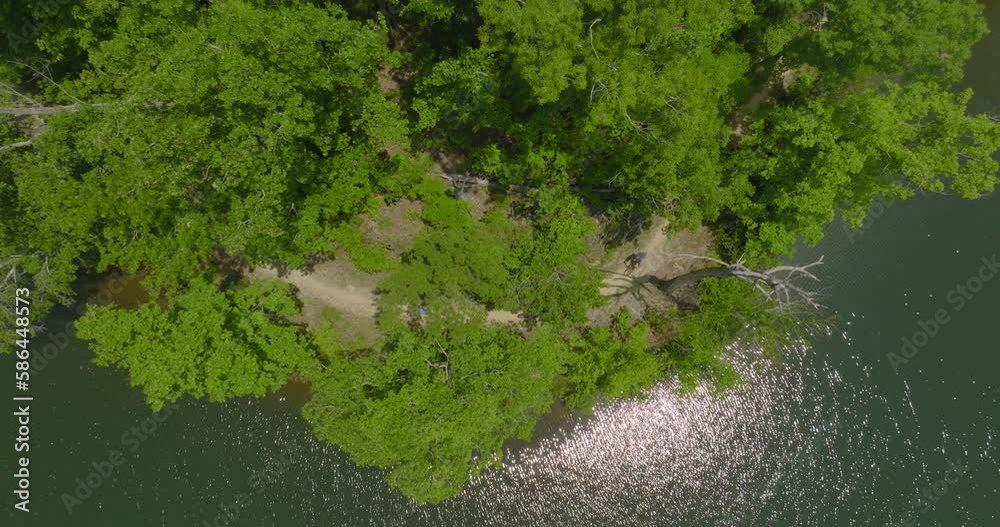Aerial: Drone Top Panning Downward Shot Of People Riding Bicycles In Forest By River On Sunny Day - Tuscaloosa, Alabama Aerial: Drone Top Panning Downward Shot Of People Riding Bicycles In Forest By River On Sunny Day - Tuscaloosa, Alabama