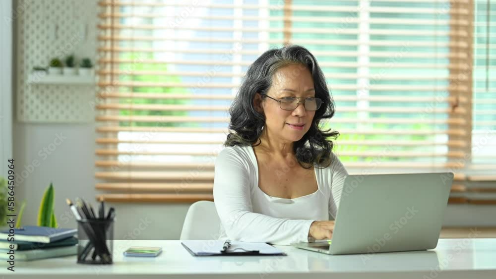 Pleasant middle aged woman looking at screen and typing on laptop computer, working online, answering emails Pleasant middle aged woman looking at screen and typing on laptop computer, working online, answering emails