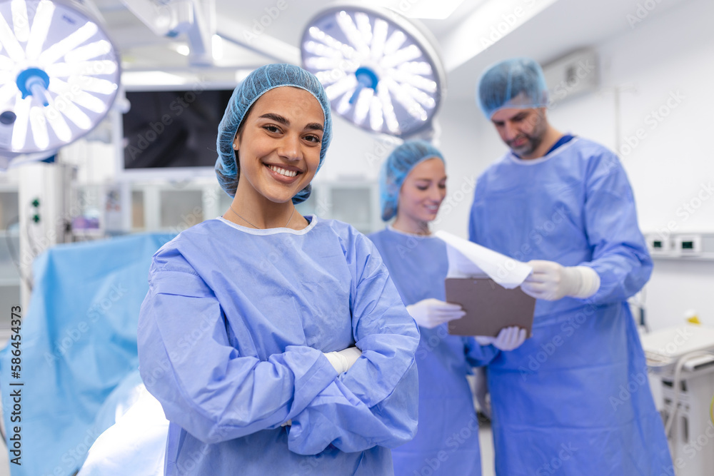 Close-up of a surgeon woman looking at camera with colleagues performing in background in operation room. The concept of medicine - obrazy, fototapety, plakaty 