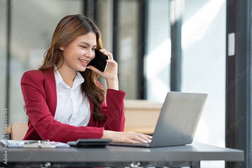 Asian businesswoman using phone to discuss business finance, taxation, marketing in real estate project and taking notes at modern office. Asian businesswoman using phone to discuss business finance, taxation, marketing in real estate project and taking notes at modern office.
