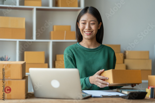 Asian female startup business owner She smiled and was delighted to receive an online order from a customer showing her information on her laptop to prepare parcels for delivery through the company. © crizzystudio