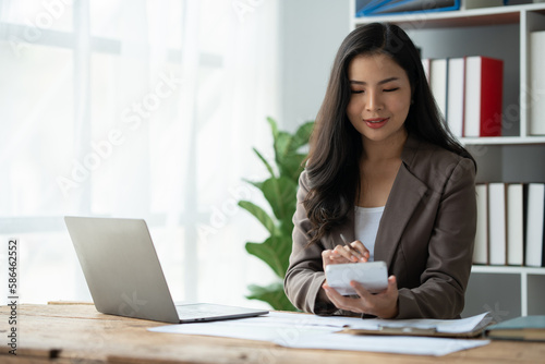Asian businesswoman recording data using desktop computer keyboard and calculator to analyze marketing strategy and real estate data reduce corporate taxes for clients. Accounting and Tax Concepts