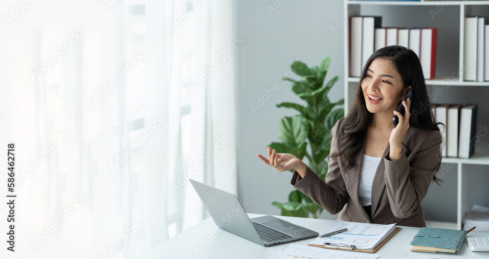 copy space, panorama ,banner , Happy young asian woman talking on the mobile phone and smiling while sitting at her working place in office. copy space, panorama ,banner , Happy young asian woman talking on the mobile phone and smiling while sitting at her working place in office.