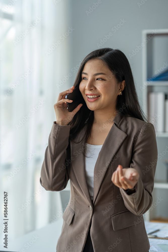 Asian business woman financially successful entrepreneur professional company executive Wearing a suit standing and talking on a mobile phone in business information in the office. Asian business woman financially successful entrepreneur professional company executive Wearing a suit standing and talking on a mobile phone in business information in the office.
