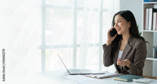 copy space, panorama ,banner , Happy young asian woman talking on the mobile phone and smiling while sitting at her working place in office.