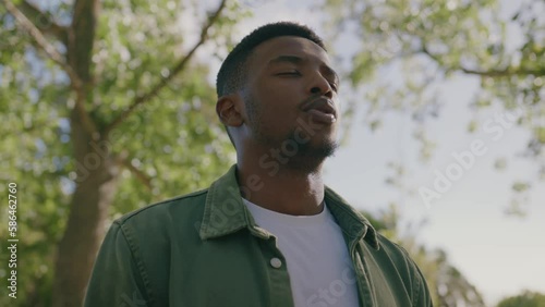 Young black man wearing shirt with eyes closed breathing under tree in park