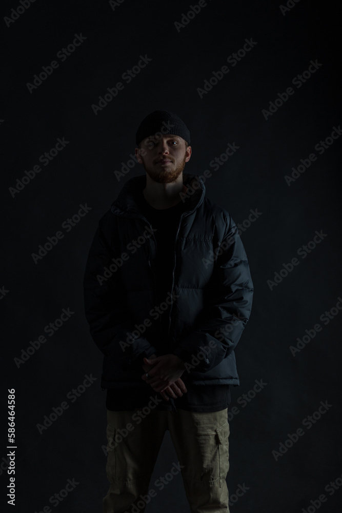 Silhouette of a fashionable guy in trendy clothes with a jacket and a hat in the dark