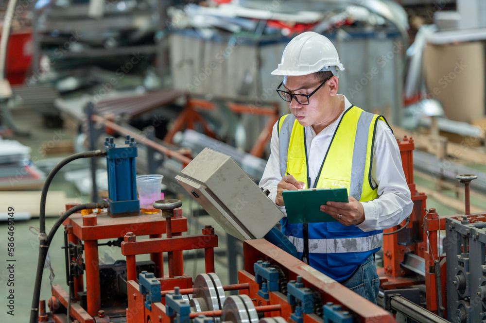Asian male engineer in uniform inspection warehouse and check control heavy machine construction installation in industrial factory. technician worker check for repair maintenance operation system Asian male engineer in uniform inspection warehouse and check control heavy machine construction installation in industrial factory. technician worker check for repair maintenance operation system