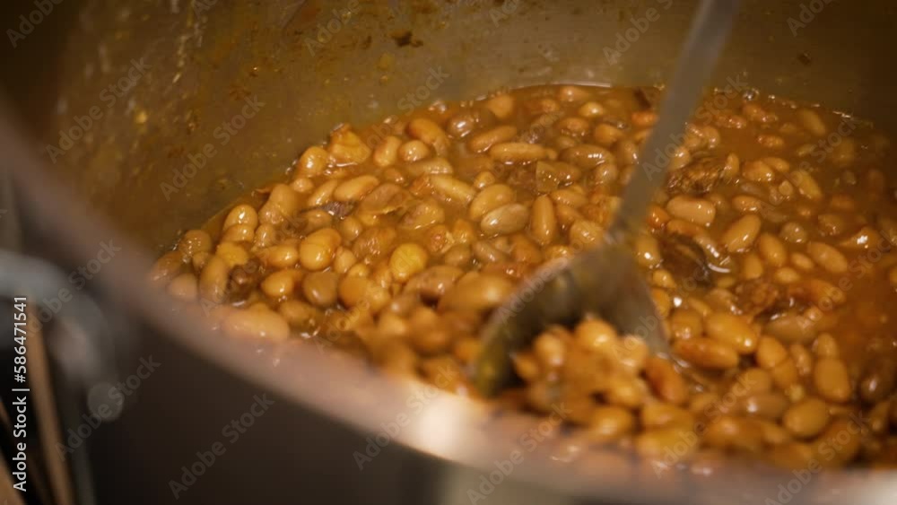 Large spoon stirs huge pot filled with barbecue pinto beans, slow motion close up 4K Large spoon stirs huge pot filled with barbecue pinto beans, slow motion close up 4K