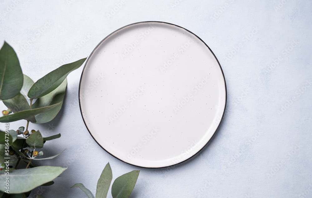 An empty plate with eucalyptus branches on a light background. Festive table setting. An empty plate with eucalyptus branches on a light background. Festive table setting.