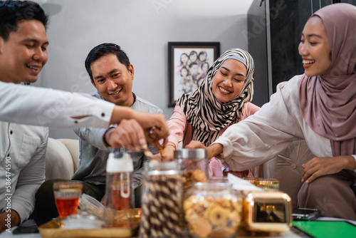 Muslim couple chatting while taking snacks from a jar during a visit to celebrate Eid at a friend's house