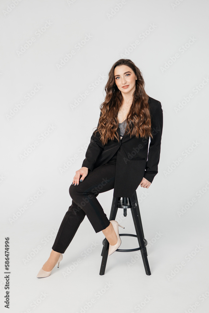 young businesswoman with long curly hair in a black suit sitting on a white background young businesswoman with long curly hair in a black suit sitting on a white background
