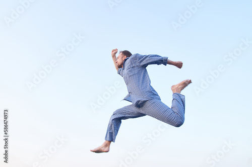 Cheerful bearded caucasian man in eyeglasses jumping in the sky outdoor in nightwear looking forward. Morning business time concept. High quality image