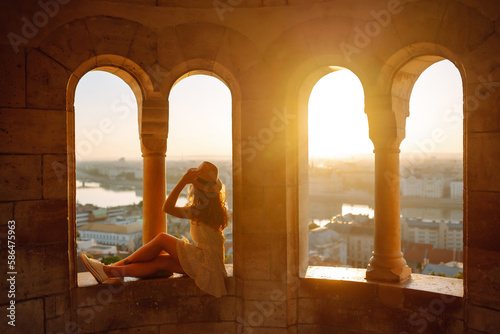 Young female tourist enjoys the view of the city at sunset. Travel and tourism concept.