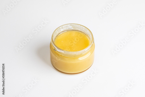 A transparent small glass jar of delicious honey, highlighted on an empty white background in close-up.