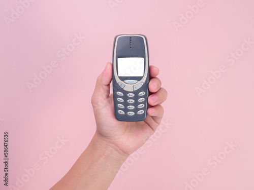 Close up hand holding mobile phone Nokia 3310 isolated on pink background. Female hand holding old used phone Nokia 3310. photo