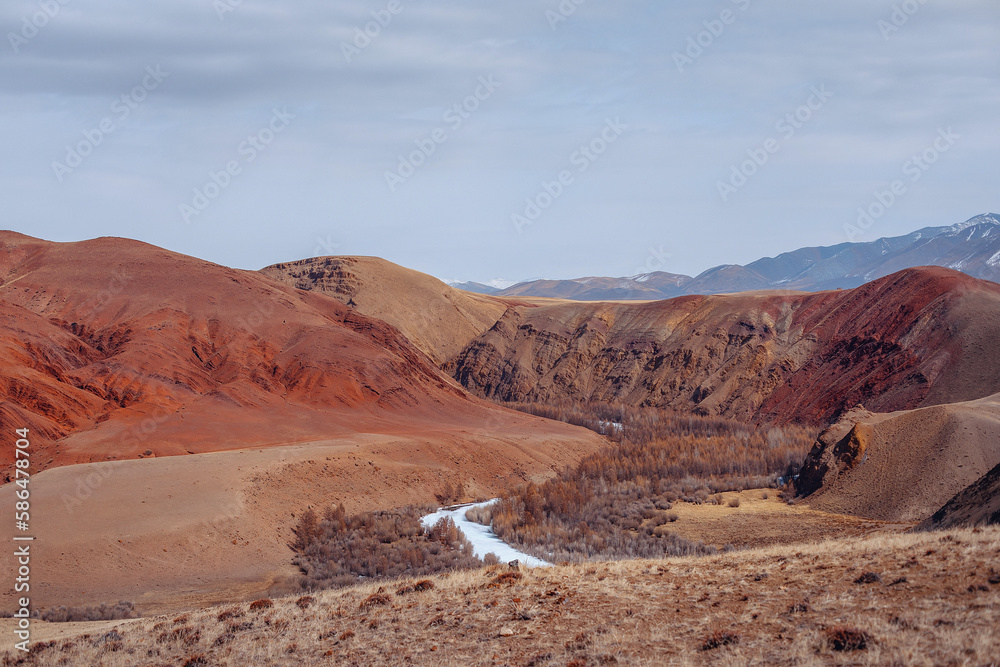 A picturesque natural landscape with red high mountains, many trees under a blue clear sky. View of relief surfaces.