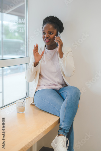 Aafrican american woman with short dark curly hair, sitting in a cafe with a mobile phone. Concept: using the phone. Mobile phone communication.