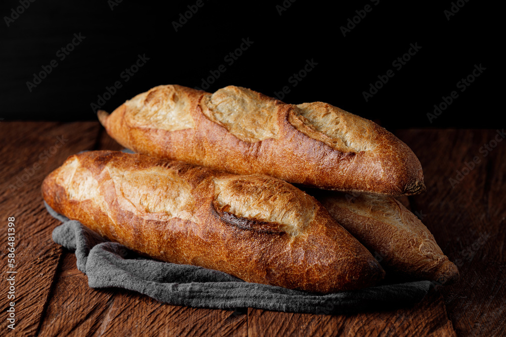 Three french baguettes on a wooden table, dark background close-up Three french baguettes on a wooden table, dark background close-up